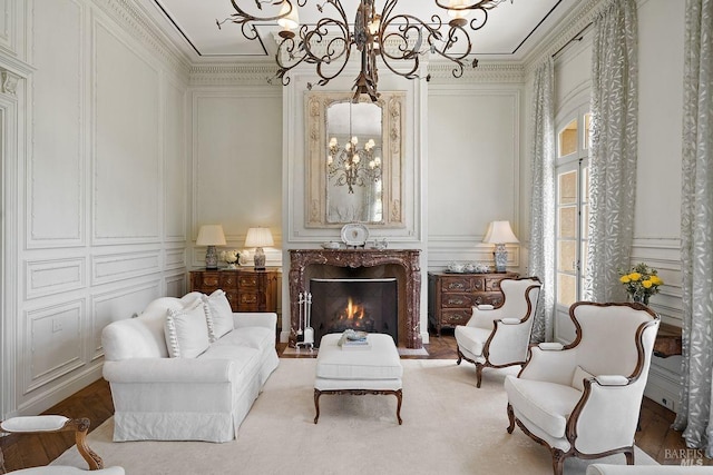 sitting room with wood-type flooring, a premium fireplace, an inviting chandelier, and crown molding