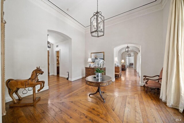 interior space with a towering ceiling, a notable chandelier, crown molding, and hardwood / wood-style flooring