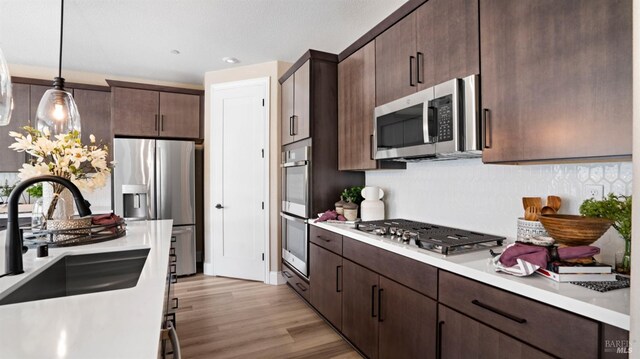 kitchen featuring appliances with stainless steel finishes, sink, dark brown cabinets, decorative light fixtures, and light wood-type flooring