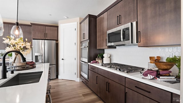 kitchen with stainless steel appliances, dark brown cabinets, sink, and pendant lighting