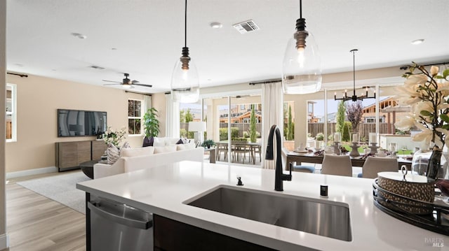 kitchen with light wood-type flooring, dishwasher, ceiling fan with notable chandelier, pendant lighting, and sink