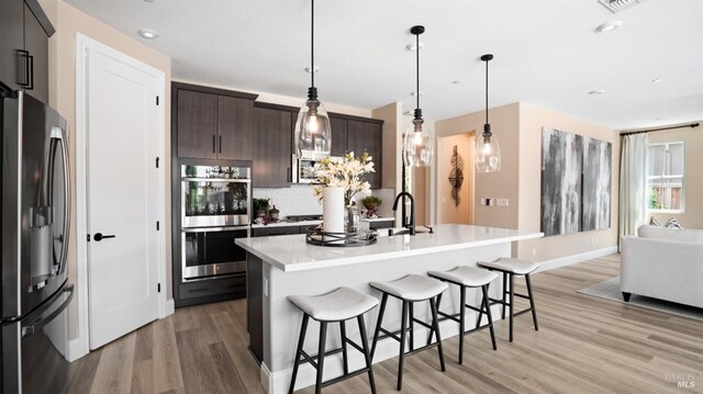 kitchen with dark brown cabinets, tasteful backsplash, stainless steel appliances, and light hardwood / wood-style floors