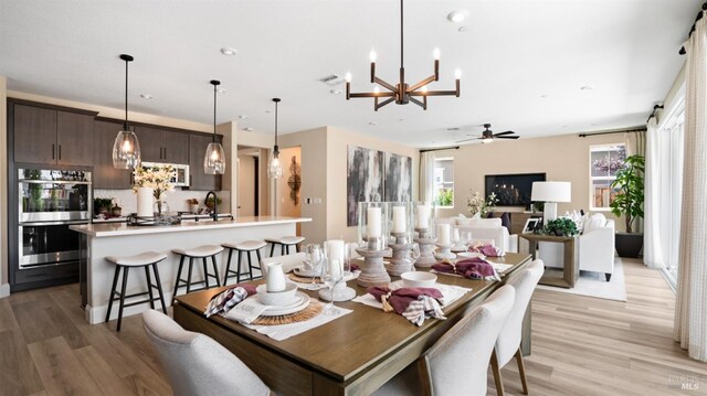 dining space with sink, light wood-type flooring, and ceiling fan with notable chandelier