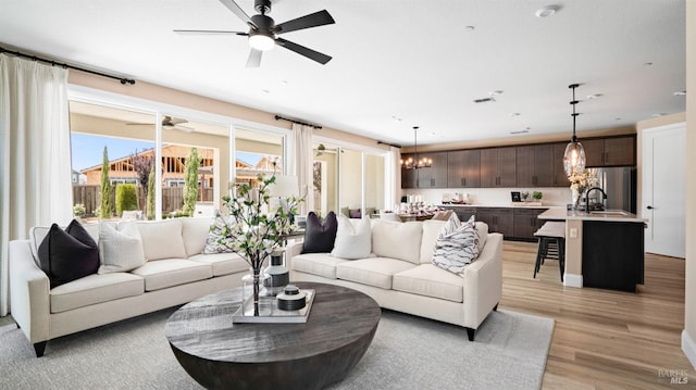 living room with ceiling fan with notable chandelier, light hardwood / wood-style flooring, and sink