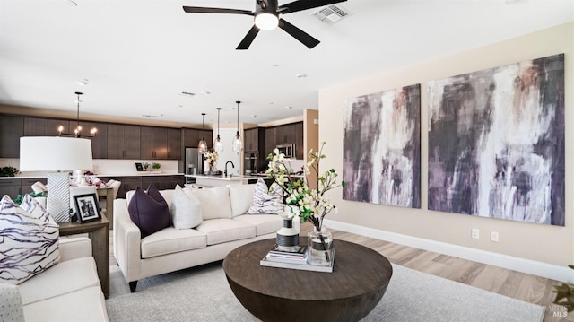 living room with sink, ceiling fan with notable chandelier, and light hardwood / wood-style flooring