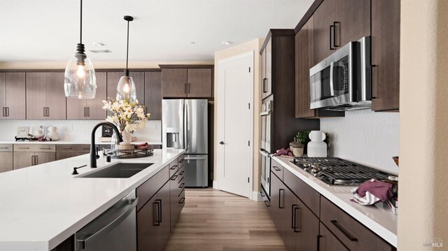 kitchen featuring tasteful backsplash, pendant lighting, sink, appliances with stainless steel finishes, and light hardwood / wood-style flooring