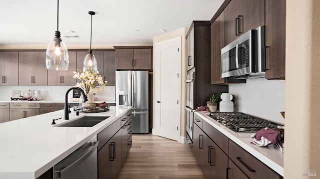 kitchen with dark brown cabinetry, sink, hanging light fixtures, stainless steel appliances, and a kitchen island with sink