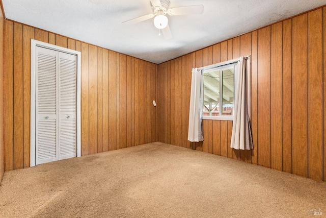 carpeted spare room featuring a ceiling fan and wooden walls