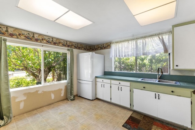 kitchen featuring freestanding refrigerator, a sink, white cabinetry, and light floors