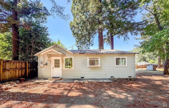 back of property with a storage unit, fence, an outdoor structure, and crawl space