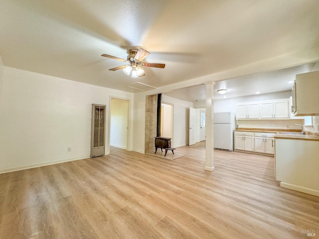 unfurnished living room with a heating unit, a wood stove, a sink, light wood finished floors, and a ceiling fan