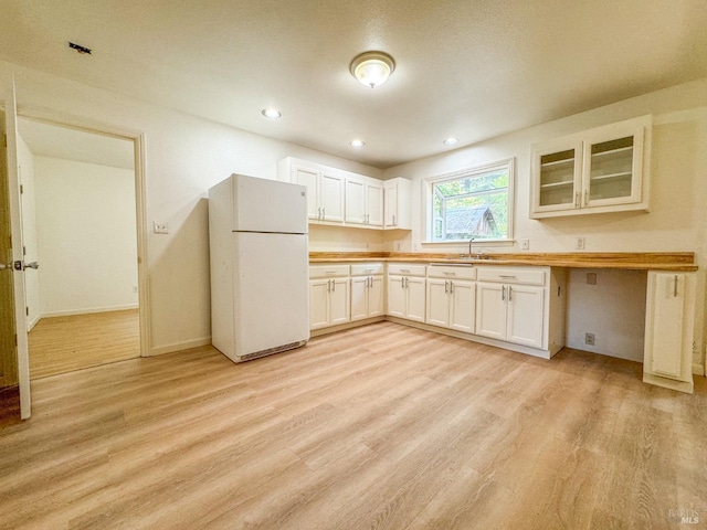kitchen with a sink, light wood-style floors, glass insert cabinets, white cabinetry, and freestanding refrigerator
