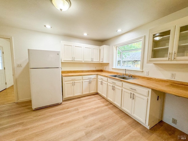 kitchen with a sink, light wood-style floors, glass insert cabinets, freestanding refrigerator, and butcher block counters