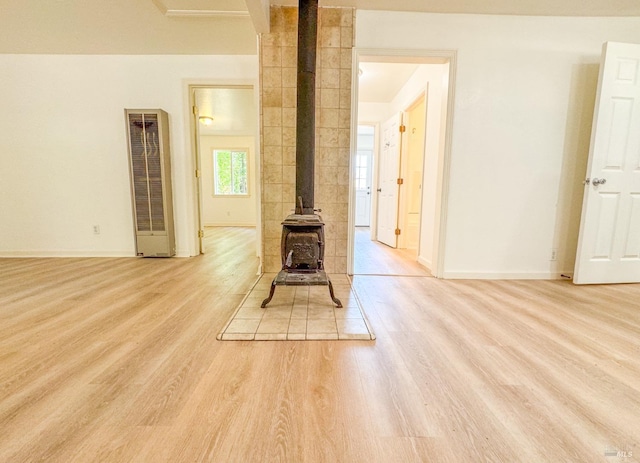 unfurnished living room with a wood stove, baseboards, light wood-style flooring, and a heating unit