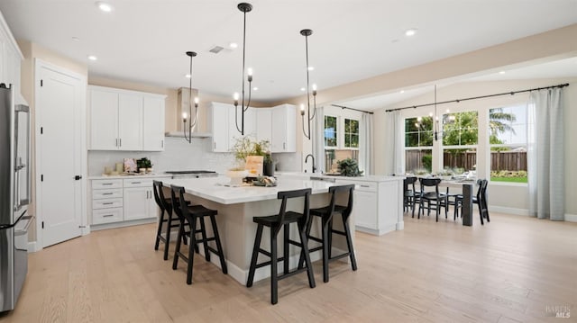 kitchen with white cabinets, light hardwood / wood-style floors, plenty of natural light, and wall chimney range hood