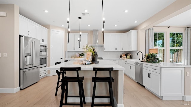 kitchen featuring stainless steel appliances, wall chimney range hood, white cabinets, light hardwood / wood-style floors, and a kitchen island