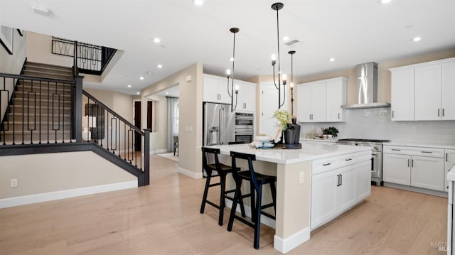 kitchen with light wood-type flooring, stainless steel appliances, wall chimney range hood, white cabinets, and a center island