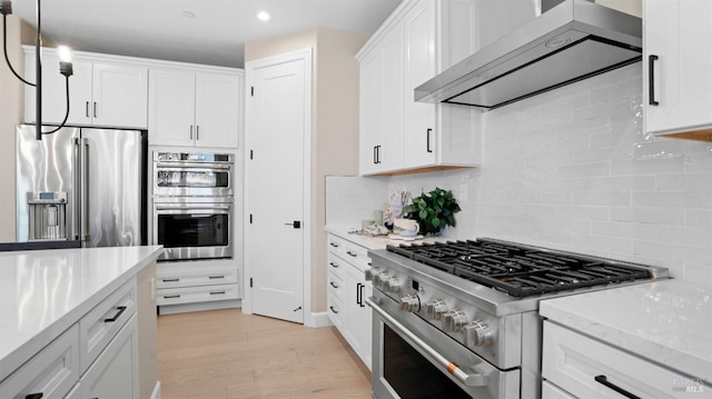 kitchen with white cabinets, wall chimney exhaust hood, premium appliances, and light hardwood / wood-style floors