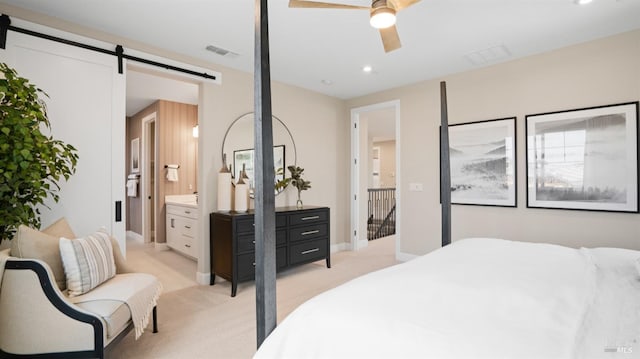 bedroom with ceiling fan, a barn door, light carpet, and connected bathroom