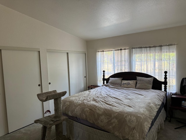 bedroom with multiple closets, vaulted ceiling, carpet floors, and a textured ceiling