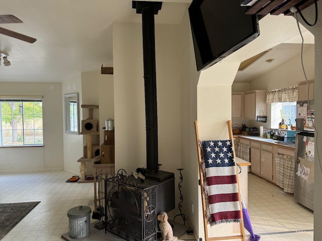 living area featuring light floors, ceiling fan, a wood stove, and plenty of natural light