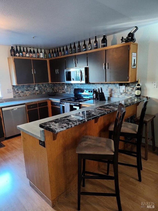 kitchen featuring kitchen peninsula, appliances with stainless steel finishes, a breakfast bar area, and light hardwood / wood-style floors