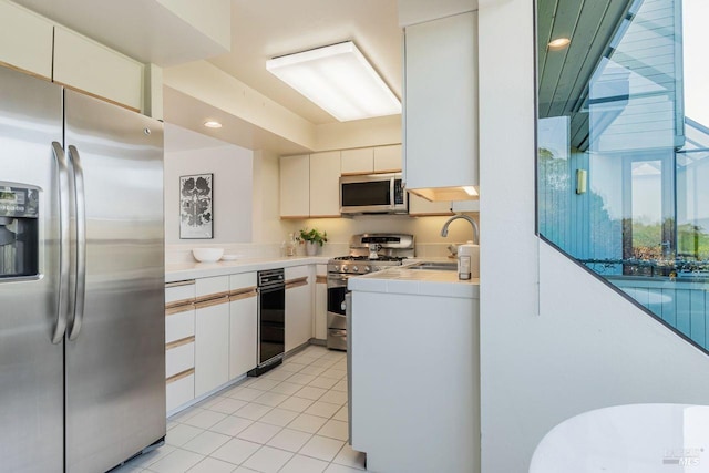 kitchen featuring stainless steel appliances, light tile patterned flooring, white cabinetry, and sink