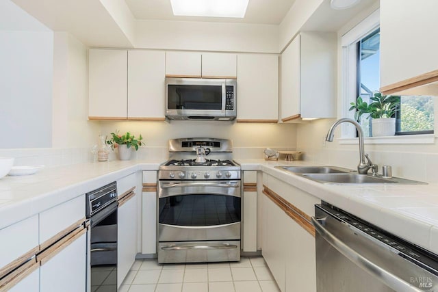 kitchen with appliances with stainless steel finishes, white cabinets, sink, and light tile patterned floors