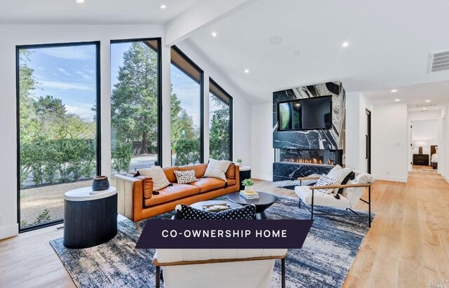 living room featuring light wood-type flooring, lofted ceiling with beams, and a high end fireplace