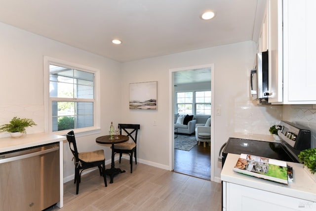 kitchen with appliances with stainless steel finishes, white cabinets, light wood-type flooring, and decorative backsplash