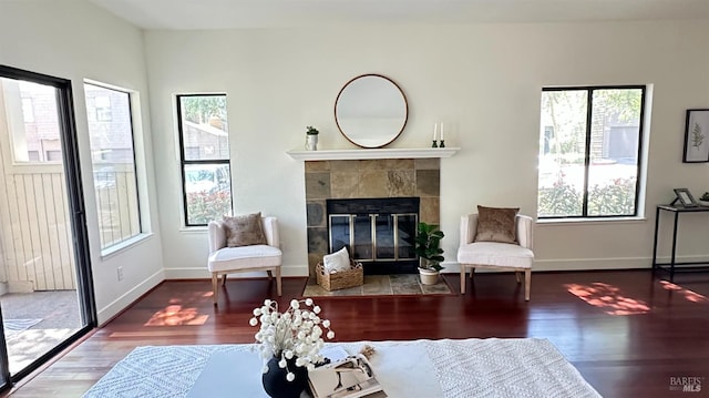 living area with baseboards, a tile fireplace, a healthy amount of sunlight, and wood finished floors