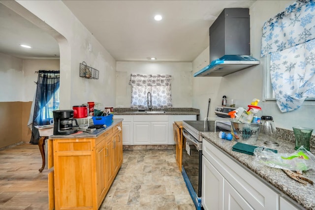 kitchen with stainless steel range with electric stovetop, wall chimney exhaust hood, sink, white cabinets, and a kitchen island