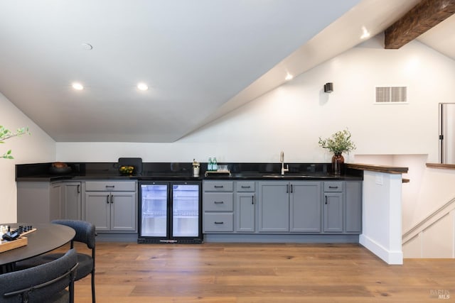 kitchen featuring sink, wood-type flooring, vaulted ceiling with beams, and beverage cooler