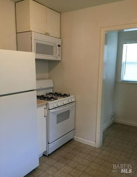 kitchen with light tile patterned flooring, white appliances, and white cabinetry