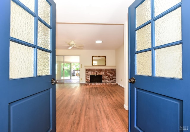 doorway to outside with hardwood / wood-style floors, a brick fireplace, and ceiling fan