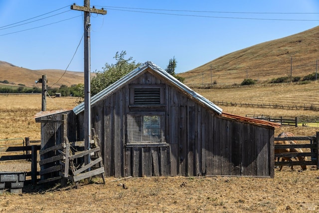 view of outbuilding featuring an outdoor structure, a mountain view, fence, and a rural view