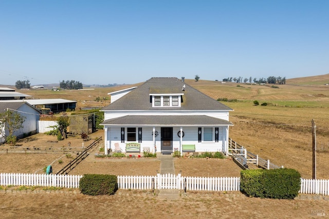 country-style home with a porch, a rural view, and a fenced front yard