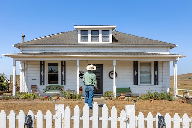 bungalow-style house with a porch, a fenced front yard, and a shingled roof