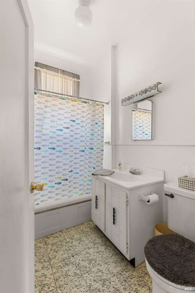 full bath featuring shower / bath combo with shower curtain, toilet, vanity, and wainscoting