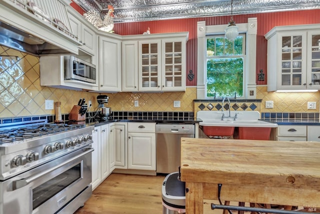 kitchen with tasteful backsplash, stainless steel appliances, pendant lighting, premium range hood, and light wood-type flooring