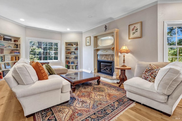 living room with ornamental molding, built in features, light wood-type flooring, and a high end fireplace