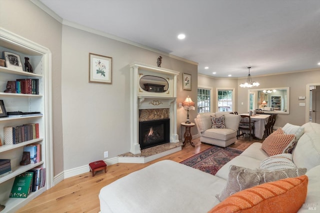 living room with hardwood / wood-style flooring, ornamental molding, a high end fireplace, and an inviting chandelier