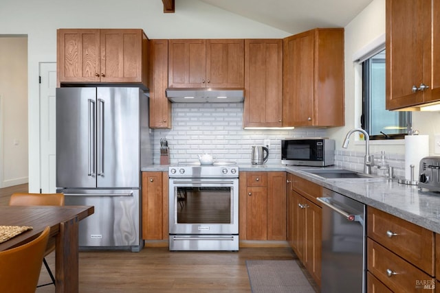 kitchen featuring sink, high end appliances, light stone countertops, range hood, and backsplash