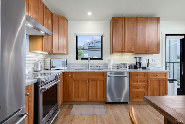 kitchen with appliances with stainless steel finishes, tasteful backsplash, sink, light stone counters, and light hardwood / wood-style flooring