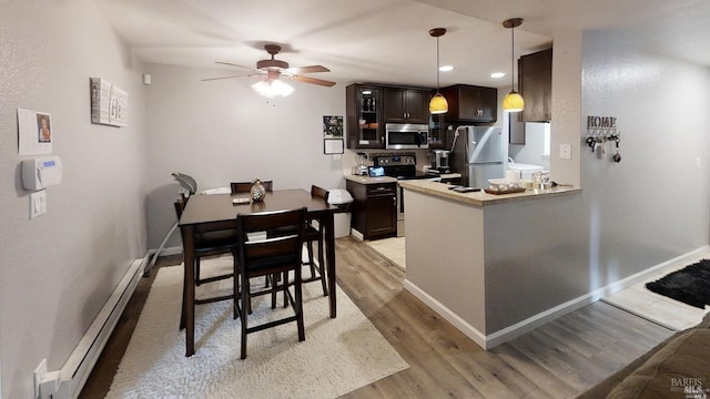 kitchen with stainless steel appliances, hanging light fixtures, a baseboard radiator, ceiling fan, and light hardwood / wood-style flooring