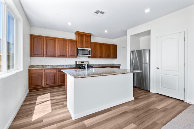 kitchen with brown cabinets, stainless steel appliances, visible vents, a sink, and an island with sink