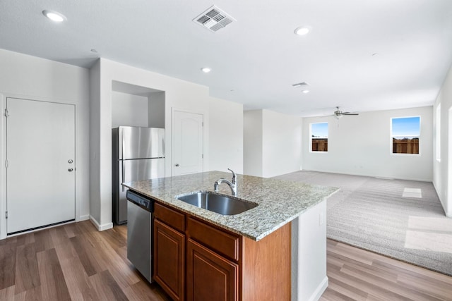 kitchen with visible vents, appliances with stainless steel finishes, open floor plan, a kitchen island with sink, and a sink