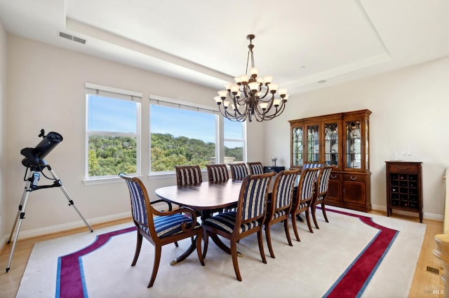 dining space featuring a tray ceiling, a chandelier, and light wood-type flooring