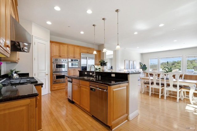 kitchen with pendant lighting, appliances with stainless steel finishes, dark stone counters, an island with sink, and sink