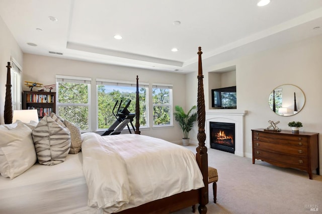 bedroom with light colored carpet, a tray ceiling, and multiple windows